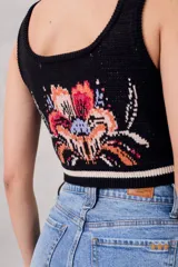 Musculosa corta de punto negra con diseño floral bordado en el frente y rayas horizontales blancas en el ruedo.