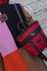 Mochila pequeña Sierra Mora en color rojo con detalles en cuero marrón. Presenta un aplique metálico de un caballo en el frente y una etiqueta de cuero con el logo de la marca. Cuenta con correas ajustables y asa superior.