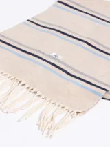 Bufanda de tejido suave en color marrón chocolate con diseño de rayas horizontales en tonos naranja, beige y gris. Presenta terminaciones con flecos en los extremos.