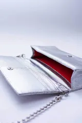 Cartera negra con textura símil cocodrilo y cadena metálica plateada.