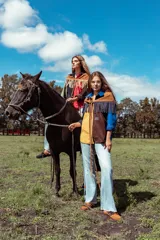 Camisa de pana de corte amplio con diseño color block, cuello camisero y mangas largas. Presenta bordados decorativos en el frente que incluyen un sol, un caballo y una bandera.