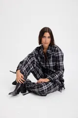 Camisa de corte holgado con estampado de cuadros en tonos marrones y beige. Presenta cuello clásico, cierre frontal con botones y mangas largas con aberturas laterales que permiten anudar la prenda en la cintura.