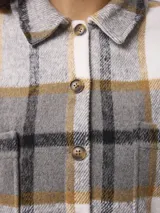 Sobrecamisa de corte holgado con estampado de cuadros en tonos gris, blanco y mostaza. Presenta cuello clásico, cierre frontal con botones, mangas largas con puños abotonados y bolsillos frontales con solapa.