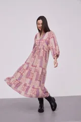 Vestido midi de viscosa con estampado patchwork en tonos rosados y violetas. Presenta cuello redondo con cordones ajustables, mangas 3/4 abullonadas y diseño holgado con falda de volados.