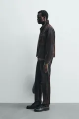 Cazadora de hombre de corte relajado, confeccionada en tejido con algodón de acabado flocado efecto terciopelo lavado, color marrón oscuro con efecto desgastado. Presenta cuello solapa, cierre frontal de cremallera, bolsillo con cremallera en el pecho y bolsillos laterales en la costura de la cadera.