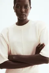 Top de punto color beige, con costura central enlazada al frente, mangas cortas con hombros caídos y ribete acanalado en el cuello, mangas y bajo.
