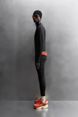 Camiseta negra de running de primera capa, confeccionada en tejido elástico y ajustado al cuerpo. Tiene cuello alto con logo estampado, mangas largas con puños ajustables y costuras planas.