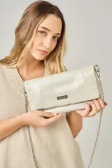 Sobre de cuero color beige con acabado brillante, diseño plegable, cierre metálico y correa de cadena plateada. Incluye placa metálica con logo de la marca Pecarí.