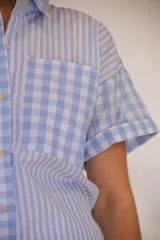 Camisa de manga corta con combinación de patrones a rayas y cuadros en tonos celeste y blanco, con bolsillo frontal aplicado y cierre de botones.