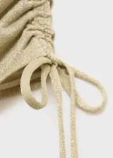 Falda corta de tejido de lúrex dorado con diseño fruncido, detalles cut-out en los laterales y cierre mediante lazos ajustables.