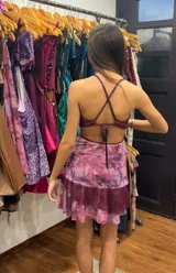 Vestido corto de tela metalizada en tono fucsia con reflejos dorados, con escote en V, diseño de top con triángulos, aberturas laterales en la cintura y doble volado irregular en el ruedo.