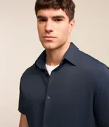 Camisa de manga corta azul marino, de corte recto con cuello camisero y cierre frontal de botones.