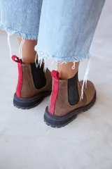 Botas Chelsea de cuero color marrón, con elásticos laterales negros, tirador trasero rojo y suela de goma negra con costuras rojas.