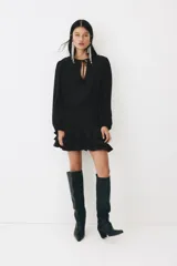 Vestido corto negro de mezcla de viscosa, con escote redondo, abertura frontal con tiras finas y mangas largas abullonadas con puños elásticos. Presenta sección entallada en la cadera con alforzas y falda corta con volados escalonados.