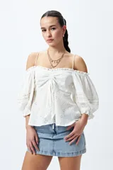 Top blanco con hombros descubiertos, bordado con detalles de puntilla y frunces en el frente. Tiene mangas abullonadas y breteles finos.