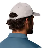 Gorra Columbia Twin Canyon Ball Cap color gris, con visera curva, ojales bordados para ventilación y un parche frontal cuadrado con el logo de la marca en negro, amarillo, marrón y blanco.