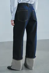 Jeans de tiro bajo y pernera ancha, confeccionados en denim azul oscuro con pespuntes en contraste. Cuentan con un diseño de cinco bolsillos, cierre frontal con cremallera y botón metálico, y destacan por su amplio doblando en el bajo que deja ver el revés de la tela con detalles de costura selvedge.