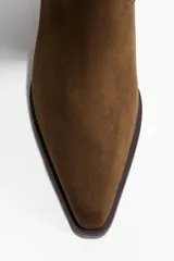 Botas de gamuza color marrón oscuro, con diseño de caña alta hasta la rodilla, punta fina, taco bajo de bloque y costuras decorativas.