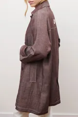 Spolverino largo de jean color azul, con cuello camisero, botones frontales y costuras decorativas en blanco.