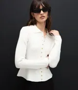 Cardigan de punto color blanco, con cuello camisero, cierre frontal de botones pequeños dorados, mangas largas y ruedo evasé con corte acinturado.