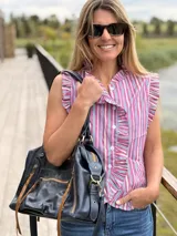Camisa sin mangas de corte recto, con diseño a rayas verticales en tonos fucsia, azul y blanco. Presenta cuello alto, cierre frontal con botones y volados fruncidos a lo largo de la botonera y en las sisas.