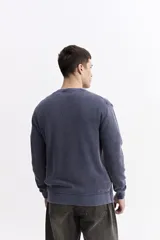 Sweater de hombre con textura waffle, color verde oliva desgastado (acid wash), cuello redondo y puños y ruedo acanalados. Presenta un pequeño logo bordado en el pecho.