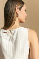 Top sin mangas color beige con finas rayas verticales negras. Presenta un diseño con lazada ajustable en el lateral de la cintura.