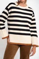 Sweater de punto con diseño a rayas horizontales en color negro y crema, de corte oversize. Presenta cuello redondo, mangas largas con puños acanalados y un detalle de borde inferior en color cobre con acabado brillante.