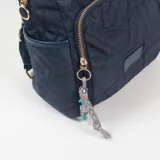 Mochila de diseño acolchado con patrón geométrico en relieve, color azul marino. Cuenta con doble asa superior, bolsillo frontal con cierre, compartimentos laterales y un colgante decorativo de cordón con cuentas de colores en el tirador del cierre.