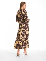 Vestido maxi de crepe con estampado floral en tonos beige y marrón oscuro. Presenta escote en V con botones frontales, mangas largas amplias con puños abotonados y cintura ajustable mediante cordón trenzado. La falda cuenta con un diseño de vuelos escalonados que aporta movimiento.