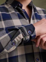 Camisa de manga larga en color azul noche con un patrón de cuadros finos en tonos rojos y verdes. Presenta cuello clásico, cierre frontal con botones y un bolsillo en el pecho con solapa.