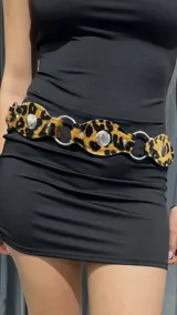 Cinturón de cuero sintético con estampado animal print, apliques metálicos plateados y argollas plateadas.