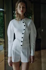 Chaqueta de punto de cuello redondo y manga larga, en color blanco, con cierre frontal asimétrico de botones negros.