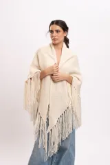 Poncho triangular de lana merino color marfil, confeccionado artesanalmente en telar manual con textura rústica y delicados flecos colgantes en los bordes.