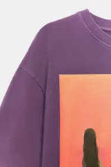 Remera oversize de algodón con efecto lavado en color violeta. Presenta cuello redondo, manga corta y una estampa frontal colorida con una ilustración artística de Manuja Waldia.