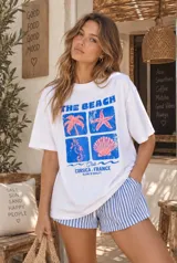 Remerón blanco de corte oversize y manga corta, con estampa frontal de temática playera en tonos azules y rosados.