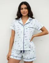 Pijama de algodón color celeste, compuesto por una camisa de manga corta con botones y un short con elástico en la cintura, ambos con detalles de ribetes oscuros y estampado de lunas y estrellas.
