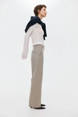 Pantalón sastrero de sarga color beige, con cintura clásica, trabillas para cinto y cierre frontal oculto. Presenta bolsillos laterales al bies, pliegues frontales y piernas rectas con raya marcada.