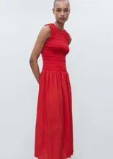Vestido largo de color rojo, sin mangas y con cuello redondo. Presenta un cuerpo superior con diseño fruncido y una falda con corte evasé.