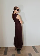 Vestido largo de encaje en color bordó, con cuello redondo, sin mangas y diseño entallado con fruncido lateral. Presenta un bajo asimétrico y cuenta con forro interior.