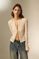 Top de encaje color natural, de manga larga y diseño holgado, con cierre frontal mediante lazos anudables y cuello redondo.