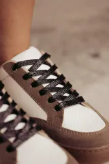 Zapatillas urbanas de cuero ecológico blanco con puntera y talón de gamuza sintética color beige. Cordones negros y suela de goma color caramelo.
