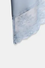 Falda midi de tejido satinado color celeste, con tiro medio y cintura elástica. El bajo tiene un acabado asimétrico con encaje combinado a tono.