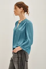 Camisa de viscosa color turquesa, de corte fluido, con cuello mao, escote en V y mangas largas abullonadas con puños elásticos.