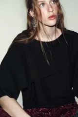 Jersey negro de punto con cuello asimétrico, manga ancha y diseño de capa superpuesta.