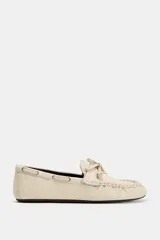 Mocasín plano de piel color beige, con diseño fruncido en la parte delantera, detalle de lazo frontal y cordón lateral entrelazado con ojalillos metálicos.