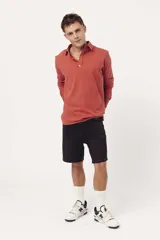 Buzo de algodón tipo polo con cuello camisero, cierre frontal con botones y mangas largas. Presenta un diseño liso en color terracota con logo bordado sutil en el pecho.
