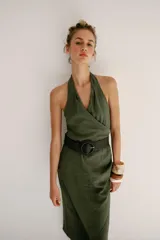 Vestido midi verde militar de cuello halter con escote en V cruzado y espalda descubierta. Cuenta con pliegues laterales, bajo asimétrico y un cinturón incorporado con hebilla redonda oscura.