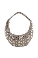 Cartera tipo hobo de diseño curvo en color beige, decorada con múltiples tachas metálicas plateadas en toda su superficie frontal. Incluye una correa de hombro fija y un dije colgante con el logo de la marca.
