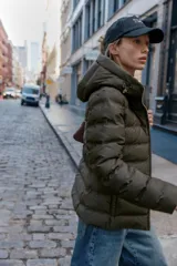 Anorak acolchado de color verde oscuro, resistente al agua y al viento. Cuenta con capucha ajustable, cierre frontal con cremallera, bolsillos laterales con cierre y cinturón elástico integrado en la cintura. El interior está forrado con un tejido efecto pelo para mayor aislamiento térmico.